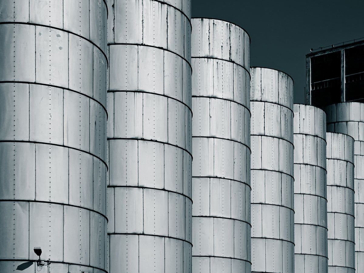 A row of steel storage silos against a dark sky.